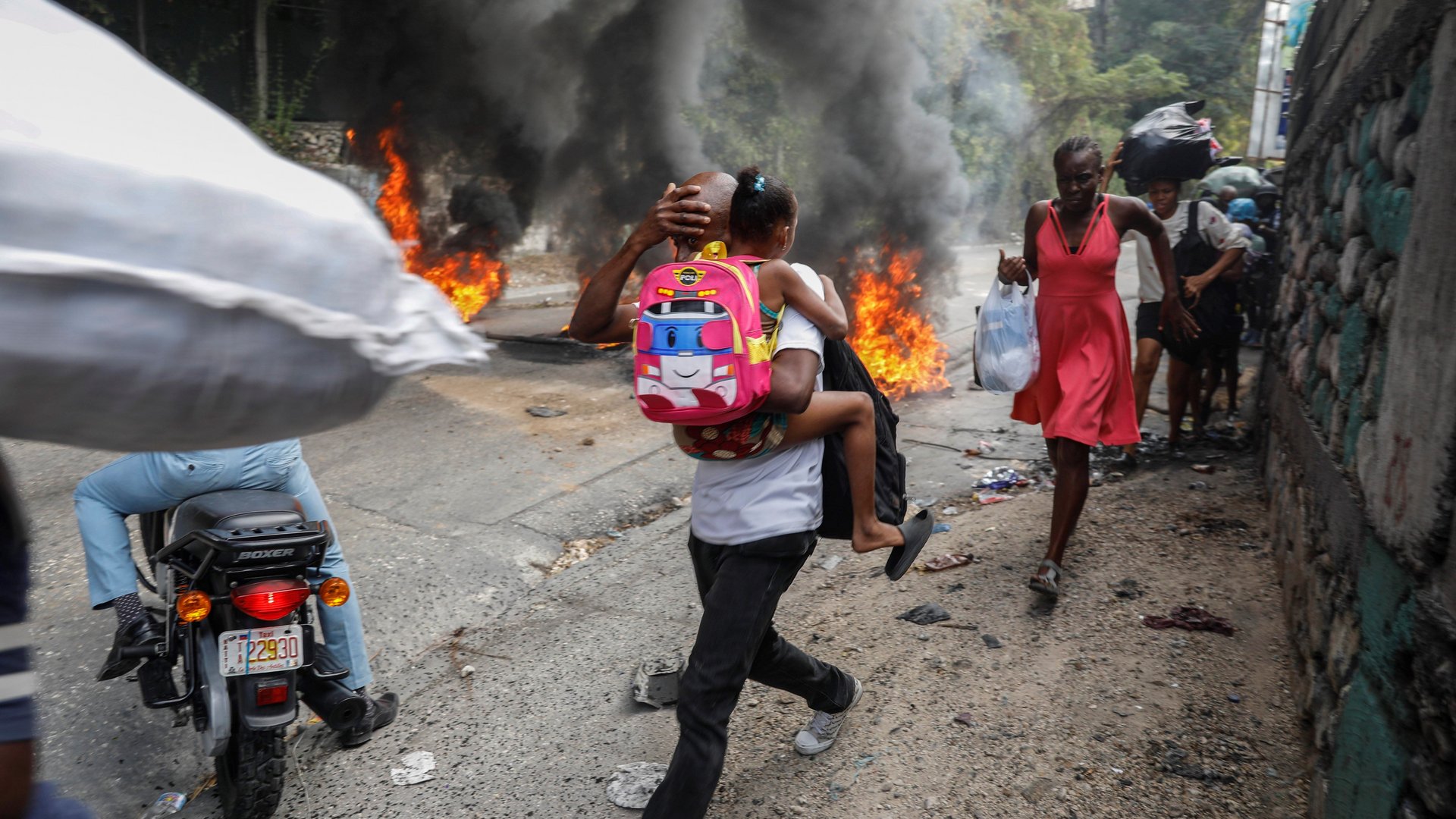 Mann trägt Kind über brennende Straße in Haiti.